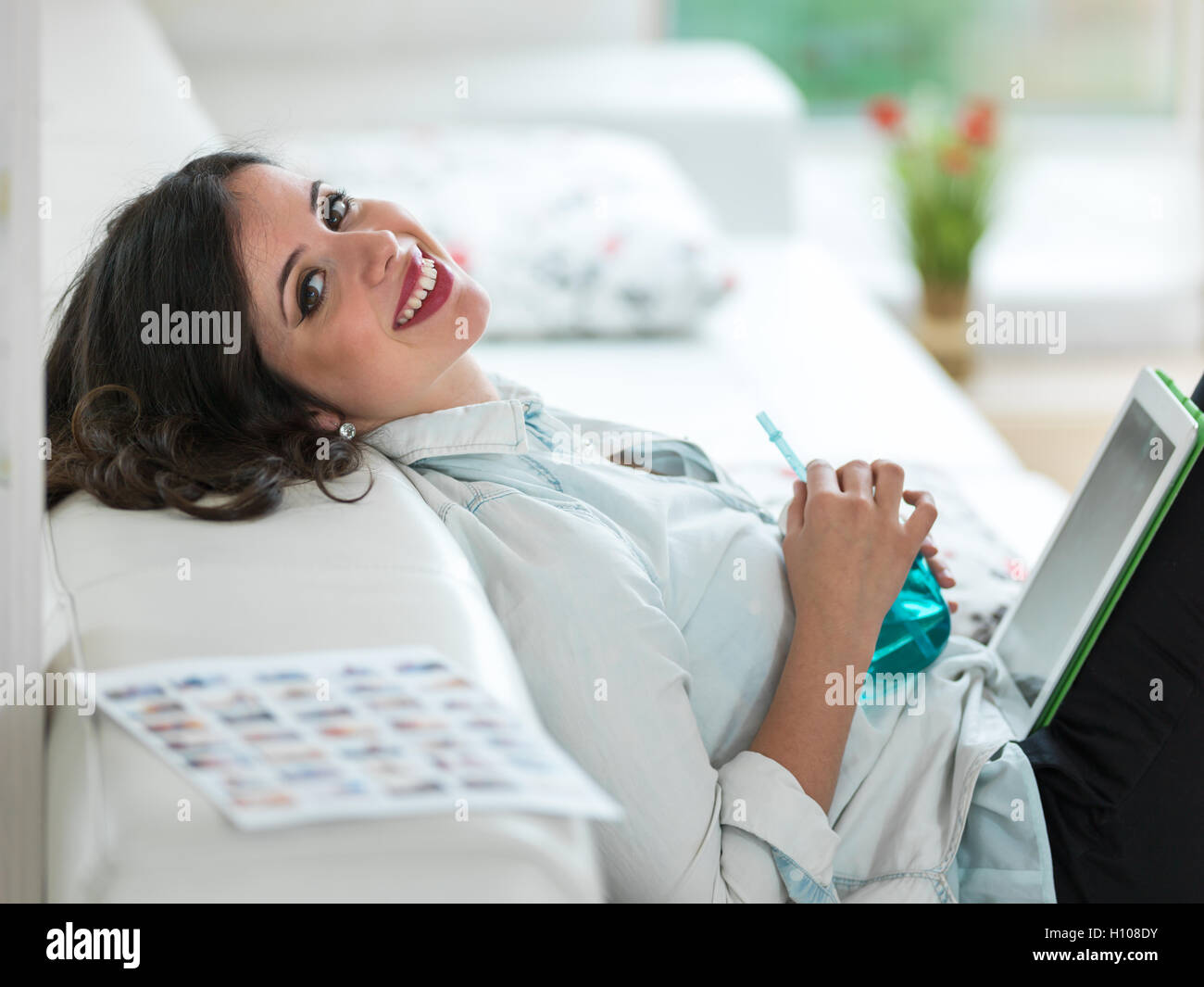Relaxed young woman sitting on sofa with tablet Stock Photo - Alamy