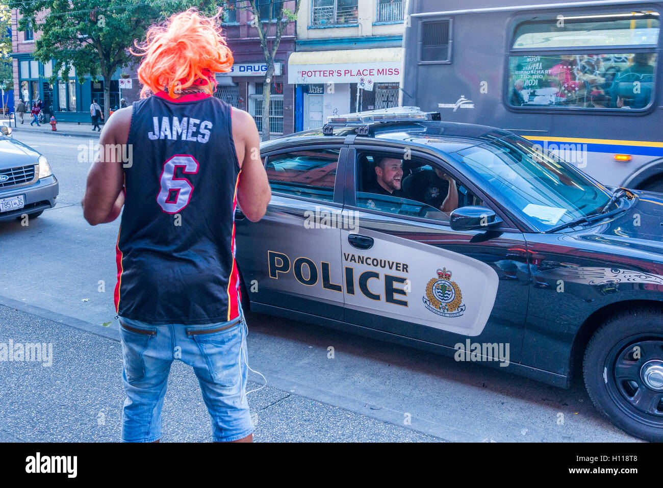 Man with orange wig converses with police officers in police car, DTES Hastings Street  Vancouver, British Columbia, Canada, Stock Photo
