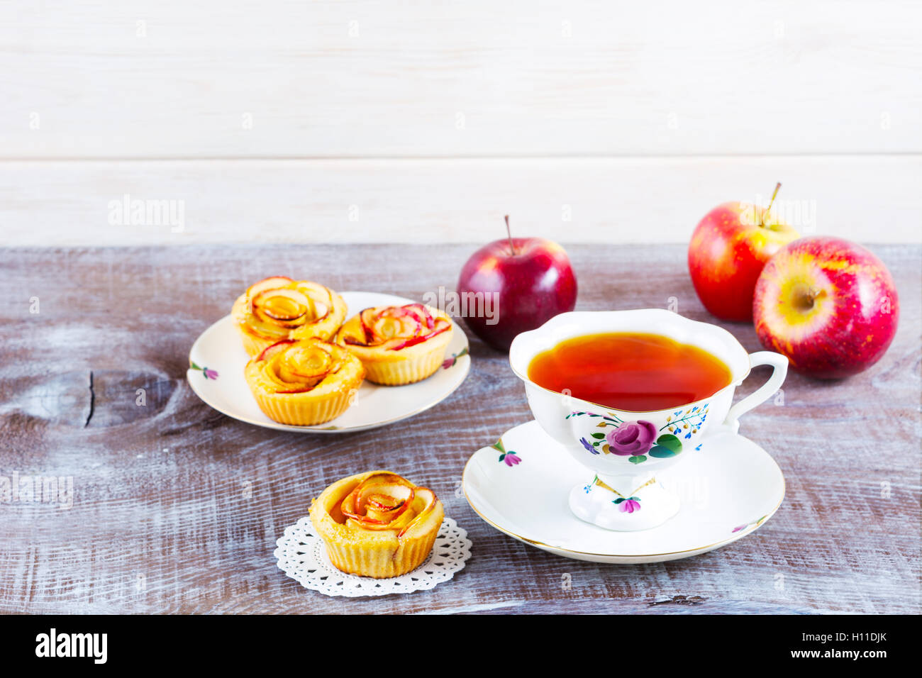 Cup of tea and apple roses shaped muffins on rustic wooden table. Sweet apple dessert pie. Homemade apple rose pastry. Breakfast Stock Photo