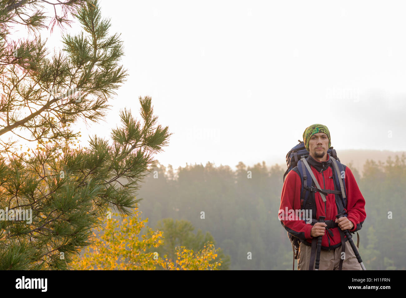 Man with backpack and trekking pole in bandana standing on a rock at dawn  on a background autumn forest Stock Photo - Alamy