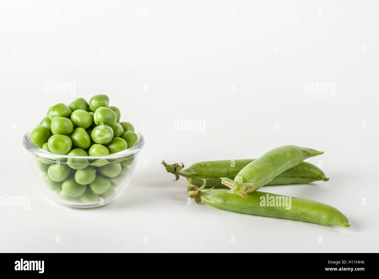 Fresh shelled green peas in a glass bowl and whole peas on white Stock Photo