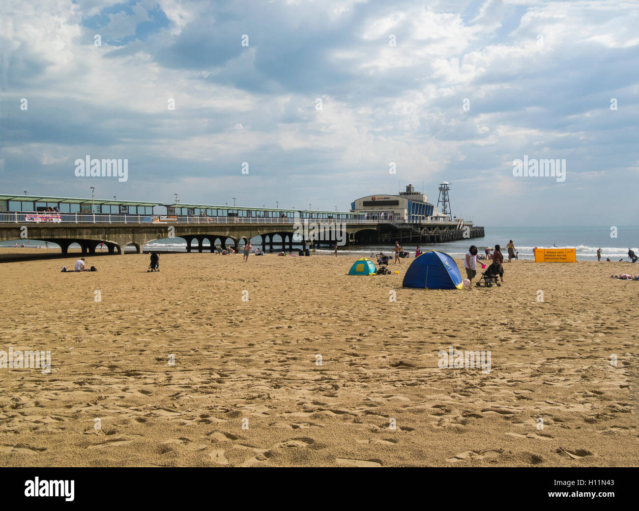 Tourists on lovely sandy beach by Bournemouth Pier stretching into Poole Bay Dorset England UK a very popular seaside town Stock Photo