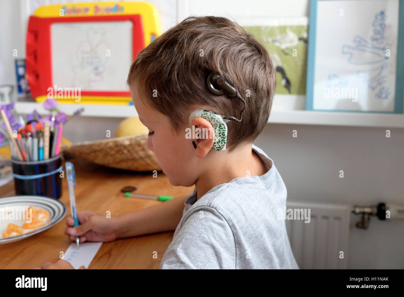 Young deaf boy student with cochlear implants aged 6 drawing writing on paper with pen sitting at table at home in Great Britain UK   KATHY DEWITT Stock Photo