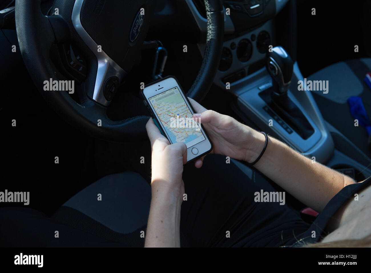 Young woman in her car using her i Phone 5s to check driving directions Stock Photo