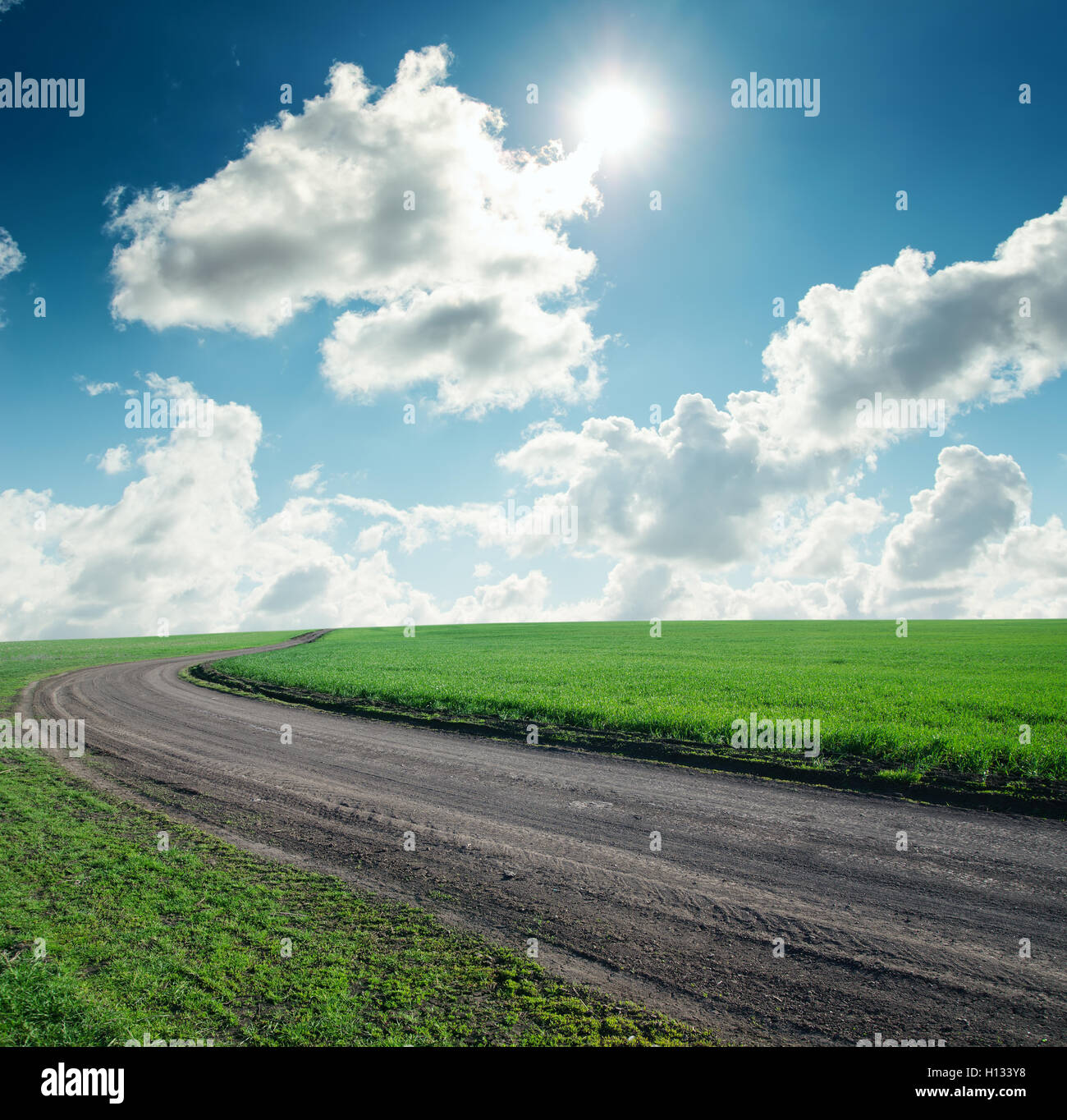 road in green grass under cloudy sky with sun Stock Photo - Alamy
