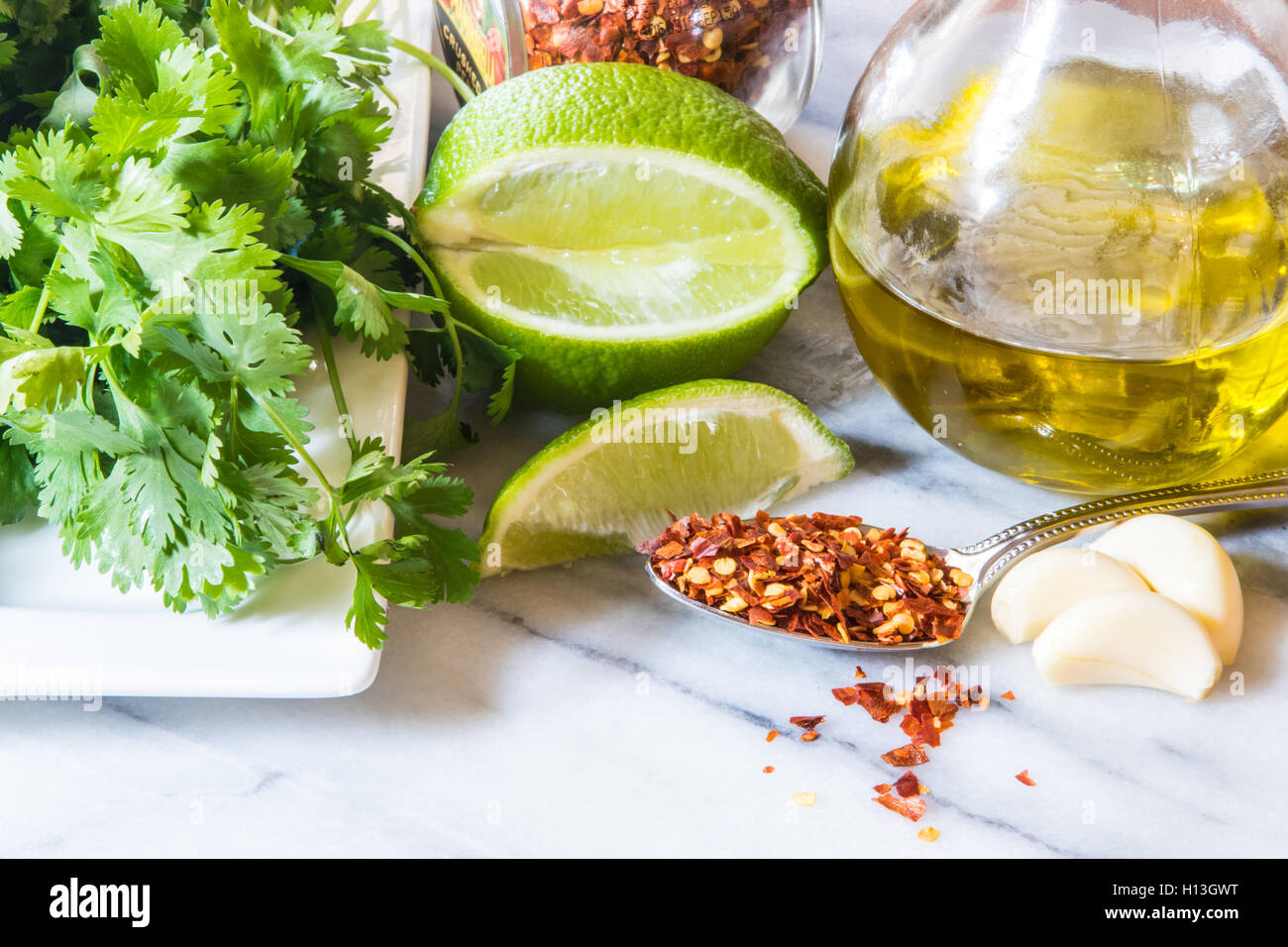 Mexican food ingredients in a kitchen on a marble top . Cilantro red pepper flakes lime garlic olive oil Stock Photo