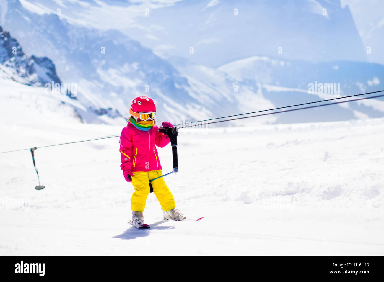 Child on a button ski lift going uphill in the mountains on a sunny