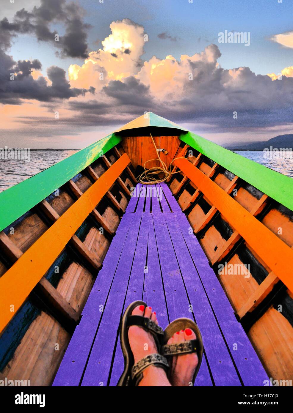 Colorful, dreamlike image showing just the feet of a female, relaxing in a rowing boat drifting towards the horizon on Inle Lake Stock Photo
