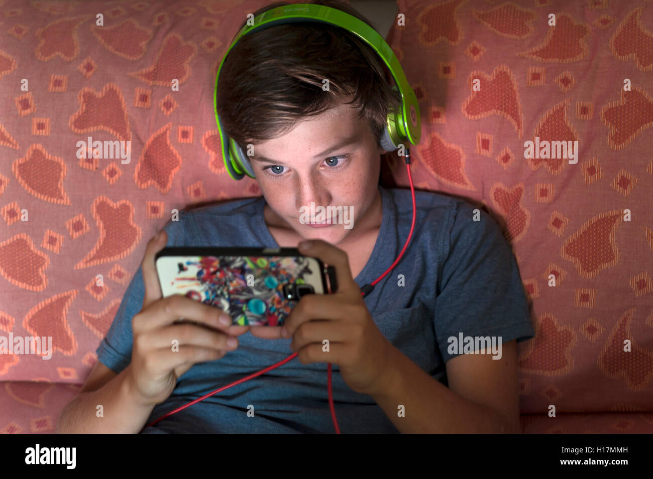 Boy, 12 years old, listening to music with headphones on a smartphone, Germany Stock Photo