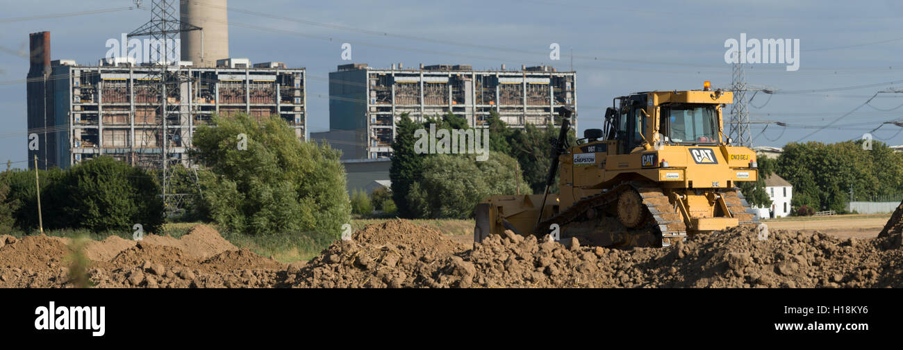 Bulldozer pushing mud over to create a wall around a new mine. With Kingsnorth Power station in the background during demolition stage. Stock Photo