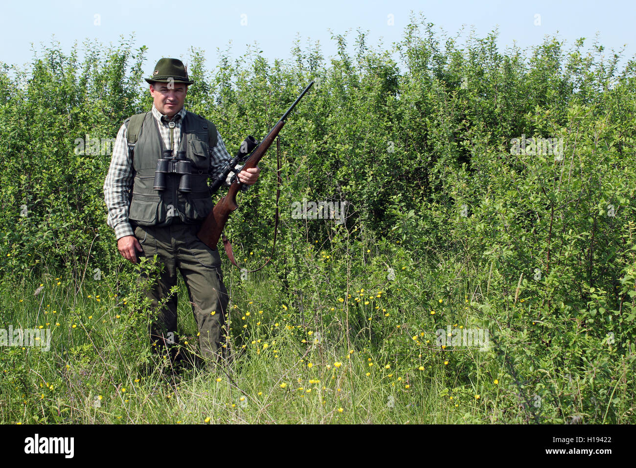 hunter with rifle standing in bush Stock Photo