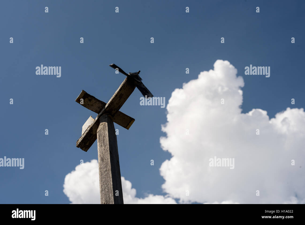 Single wooden airplane weather vane set against a blue sky with a large white cloud. Stock Photo