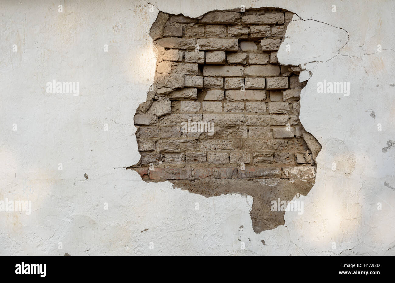 Large crumbling patch of missing paintwork on a white wall with the bricks underneath visible due to the gap. Stock Photo