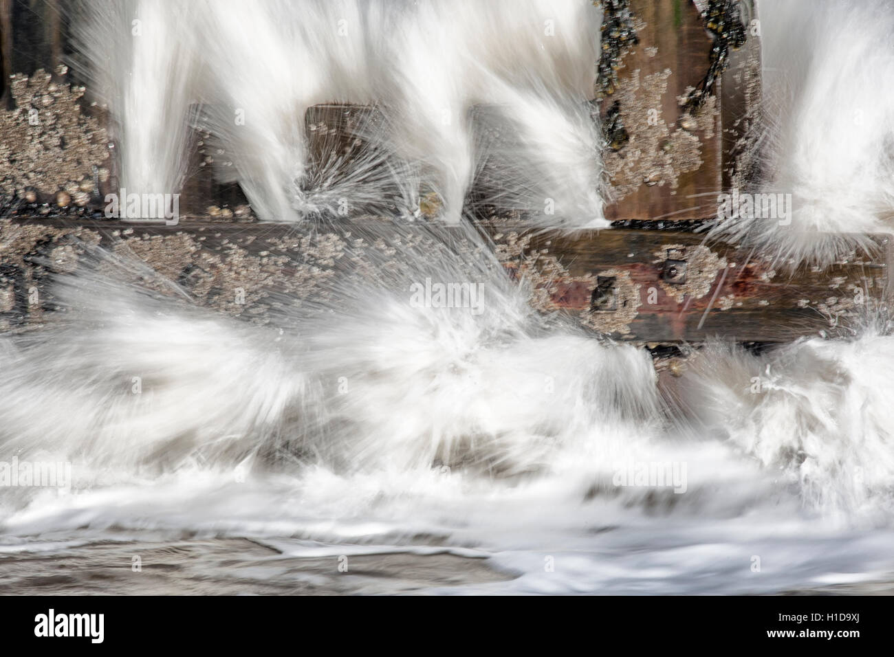 Sea water breaking through groynes on beach in slow motion Stock Photo
