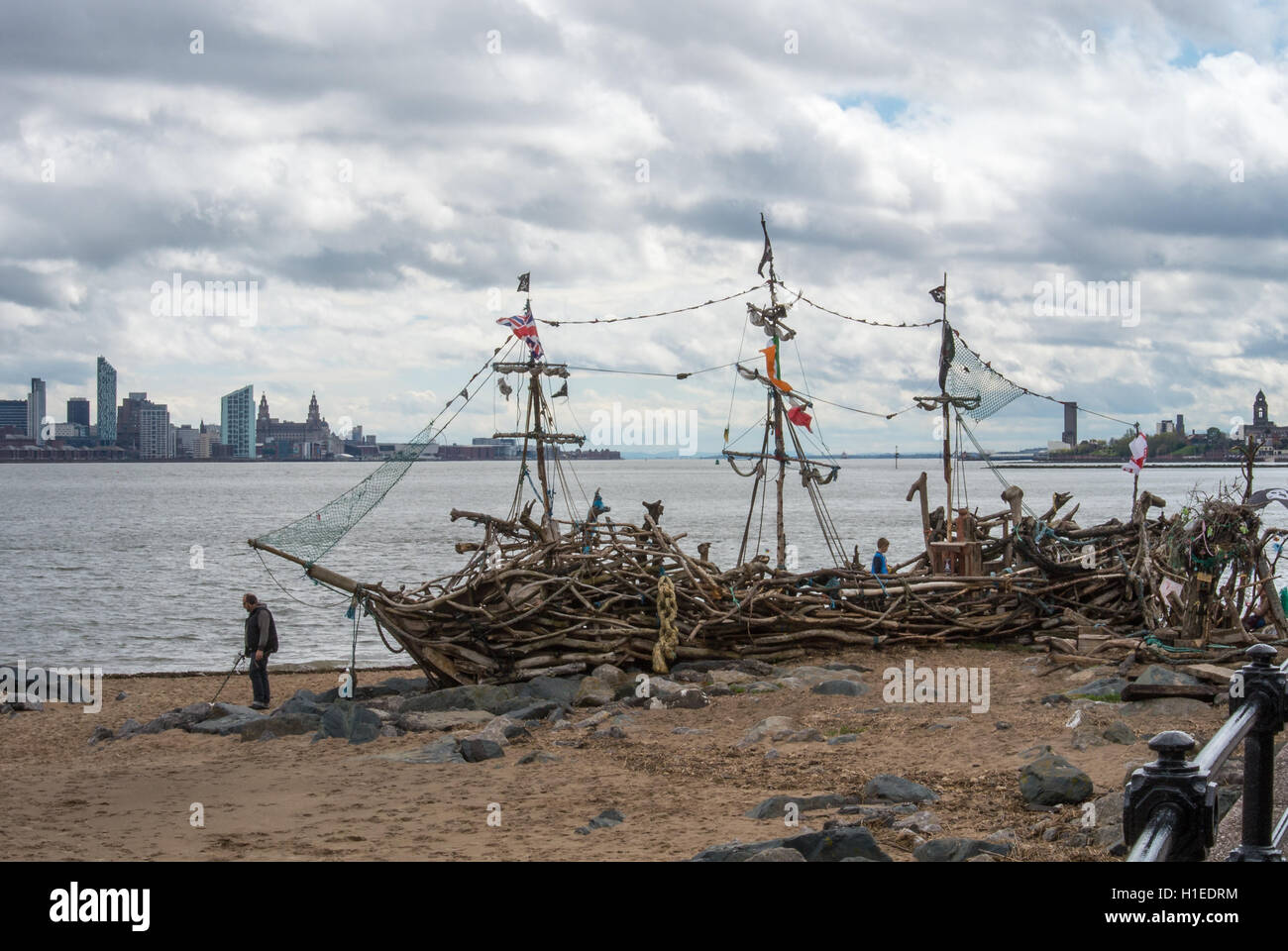 A man with a metal detector looks for treasure next to the Black Pearl ship New Brighton with Liverpool skyline Stock Photo