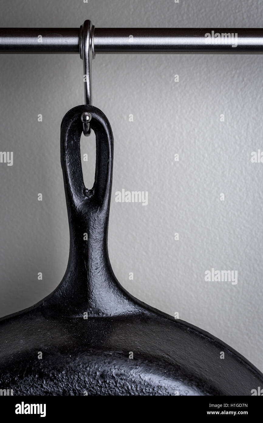 Vintage cast iron frying pan hanging on display from metal hook and rod