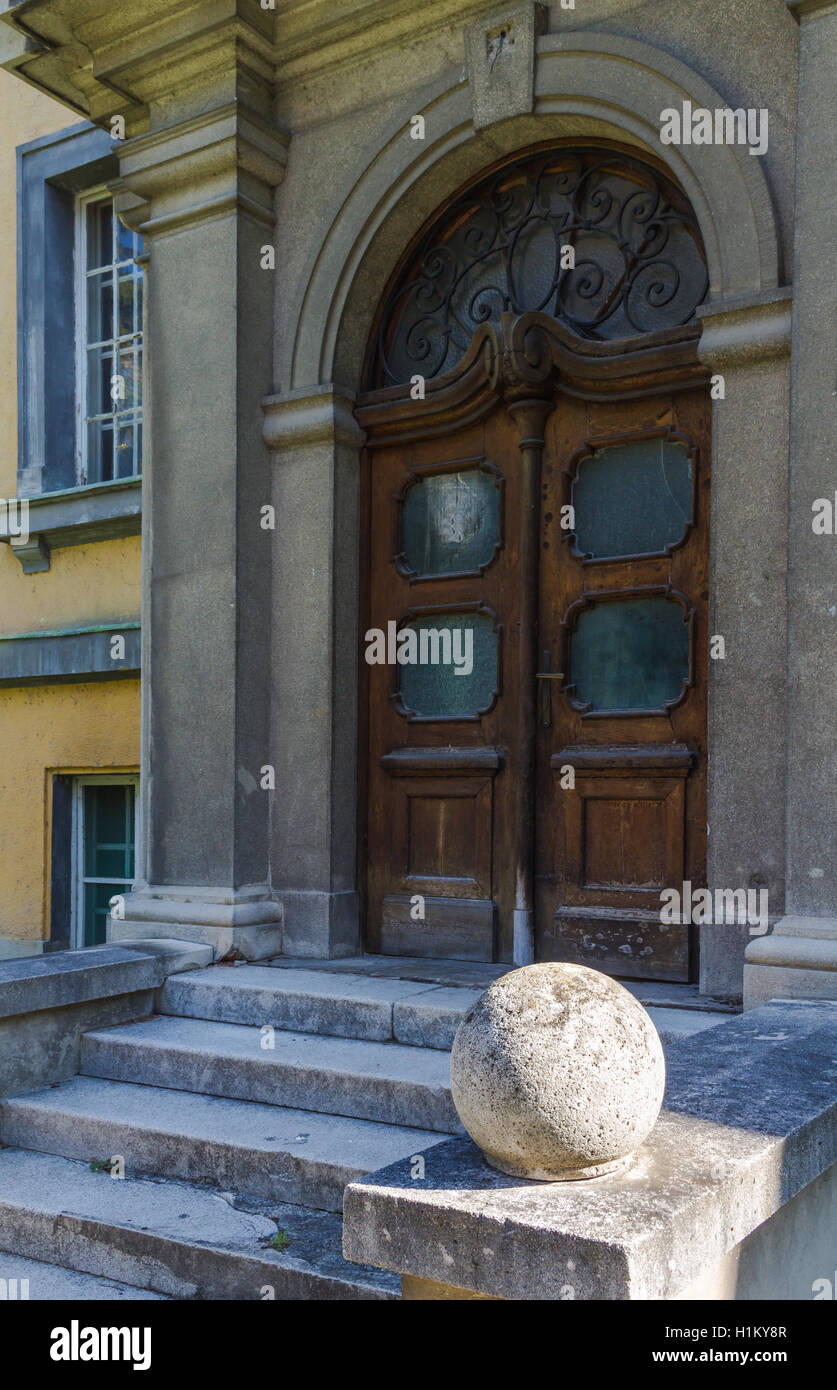Side view on the entrance to an old building. Heavy wooden door with an arch. Stairs in a shadow and a stone ball enlightened. Stock Photo