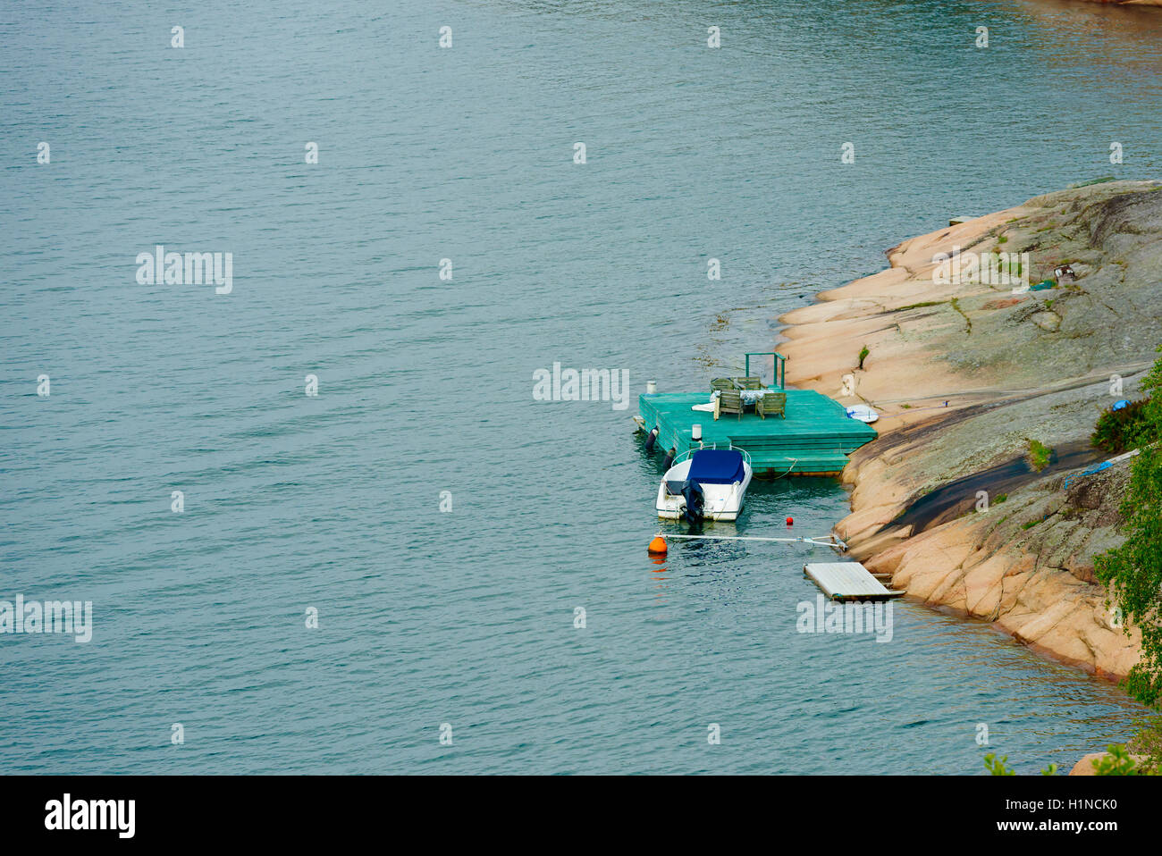 Small motorboat moored at green wooden pier in Swedish west coast landscape. Stock Photo