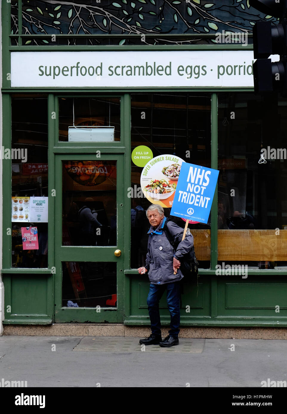 A lone, elderly man holds a placard in support of the NHS as he rests outside a London Cafe Stock Photo