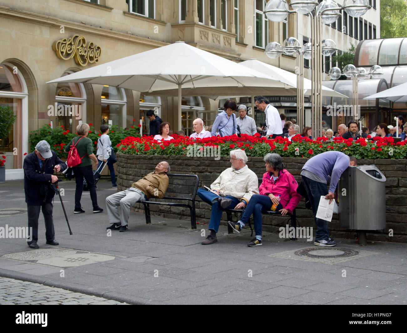 Street scene in the city center of Cologne, Germany, with man sticking his head in a garbage bin. Stock Photo