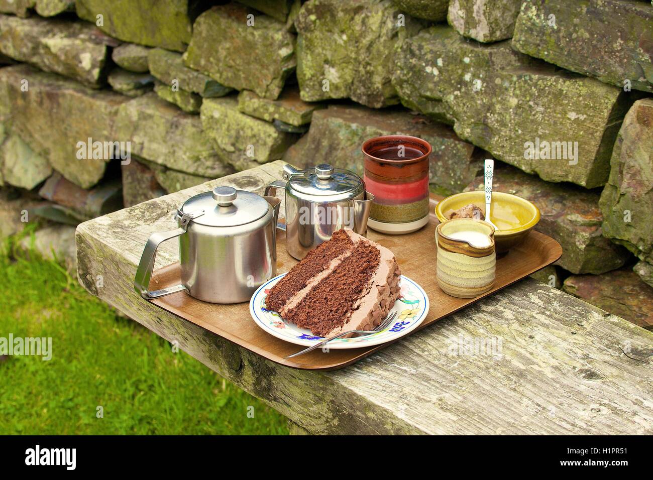 Tea and chocolate cake on a tray on a bench outside. Mosedale Coffee Shop, Quaker Meeting House, Mosedale, Cumbria, England, UK. Stock Photo