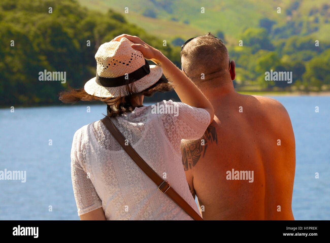 Couple looking at the view over a lake with the woman holding Panama hat on. Ullswater, Penrith, The Lake District National Park Stock Photo