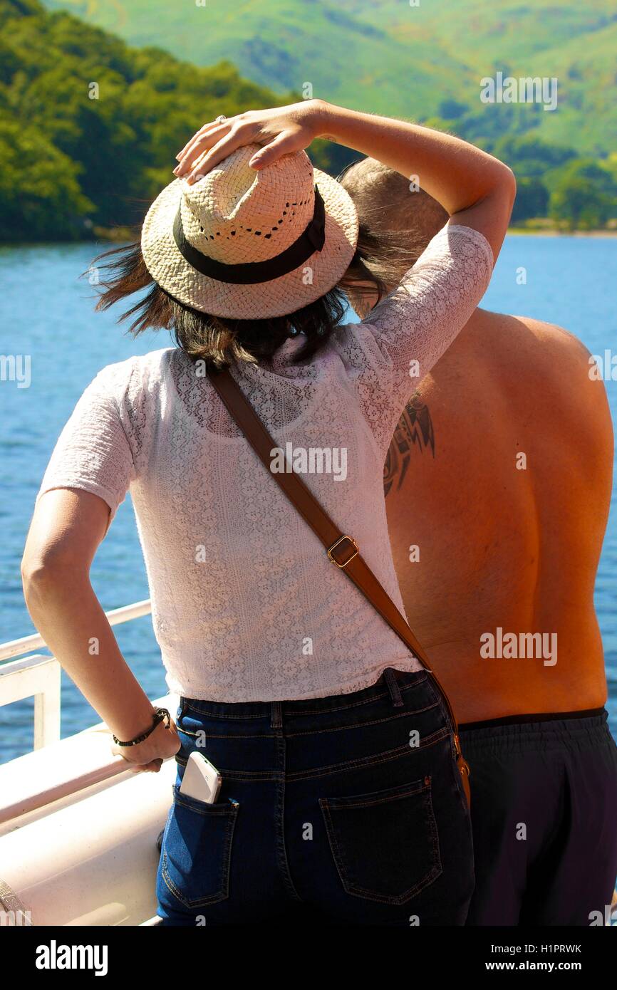 Couple looking at the view over a lake with the woman holding Panama hat on. Ullswater, Penrith, The Lake District National Park Stock Photo