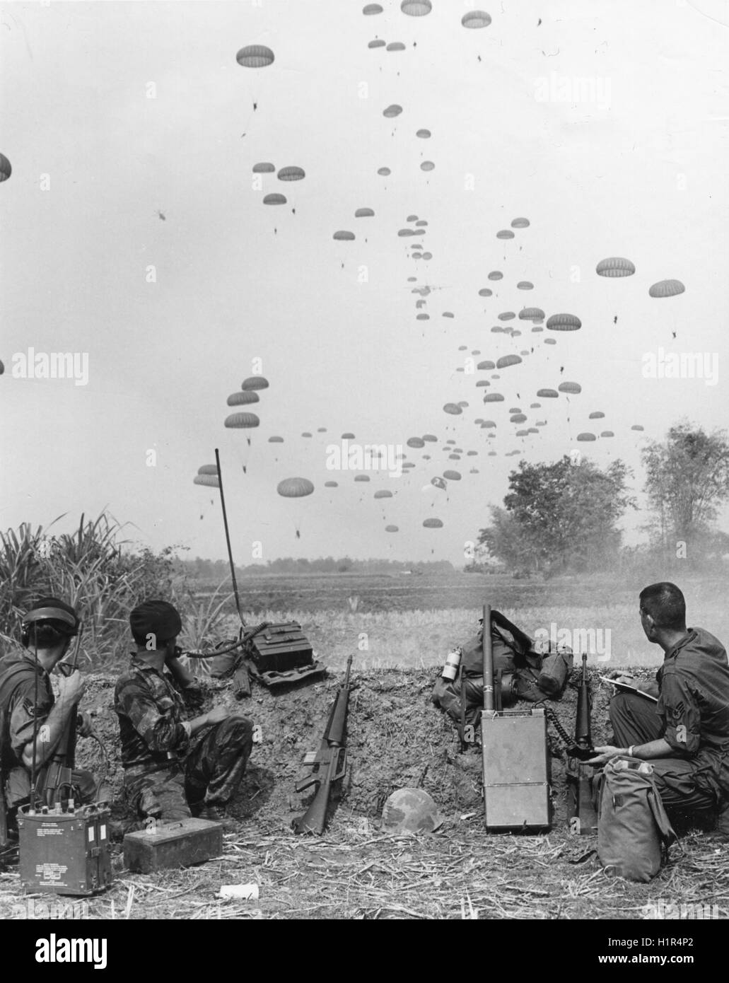 Members of the First US Air Force Combat Control Team watch paratroopers of the Army of Vietnam Airborne Division drop into a Viet Cong infiltrated area. Stock Photo
