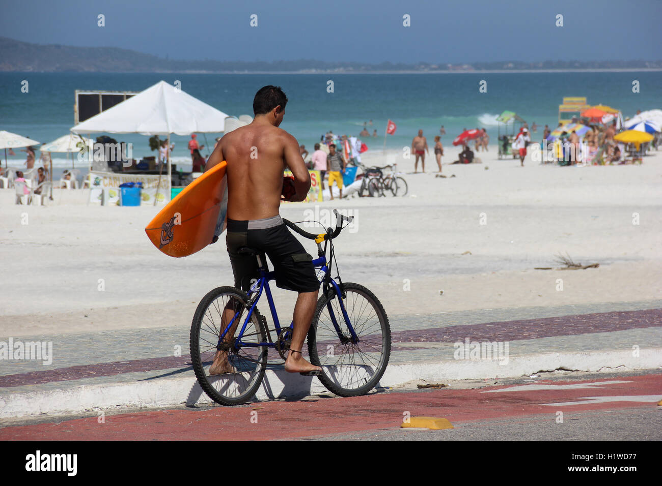 Man carrying his surfboard on a bike while watching the sea on a sunny
