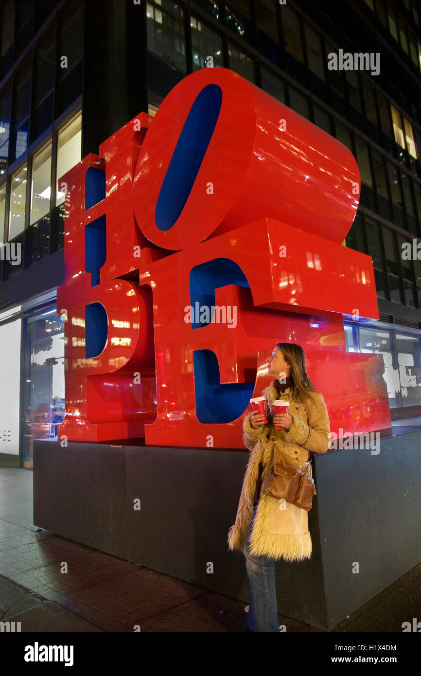 Beautiful Middle-Aged Caucasian Woman Holds Two Coffees Waiting for Her Lover Standing Beside Red HOPE Sculpture in Manhattan, New York City, USA Stock Photo