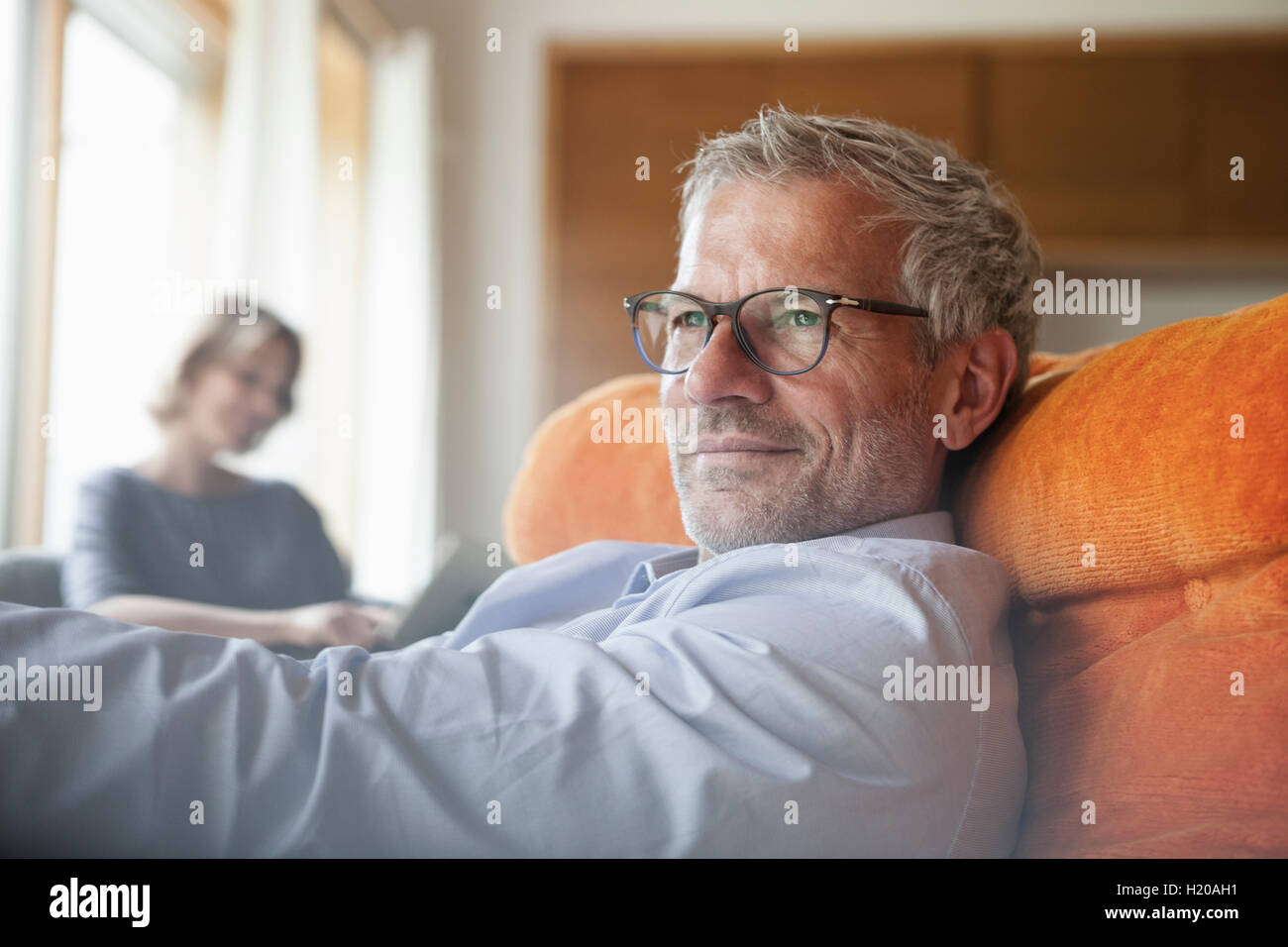 Man relaxing in armchair with wife in background Stock Photo Alamy