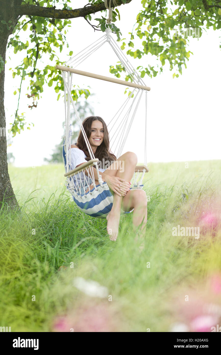 Happy woman relaxing in a hanging chair under a tree Stock Photo - Alamy