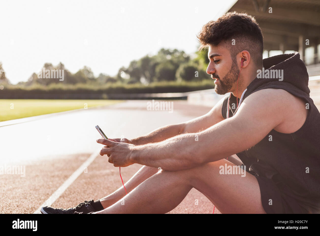 Young man with cell phone sitting on tartan track Stock Photo