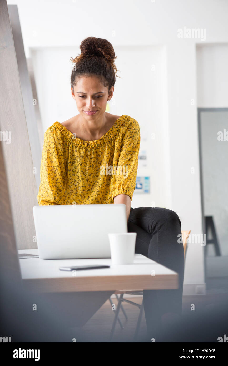 Smiling woman sitting on office desk using laptop Stock Photo