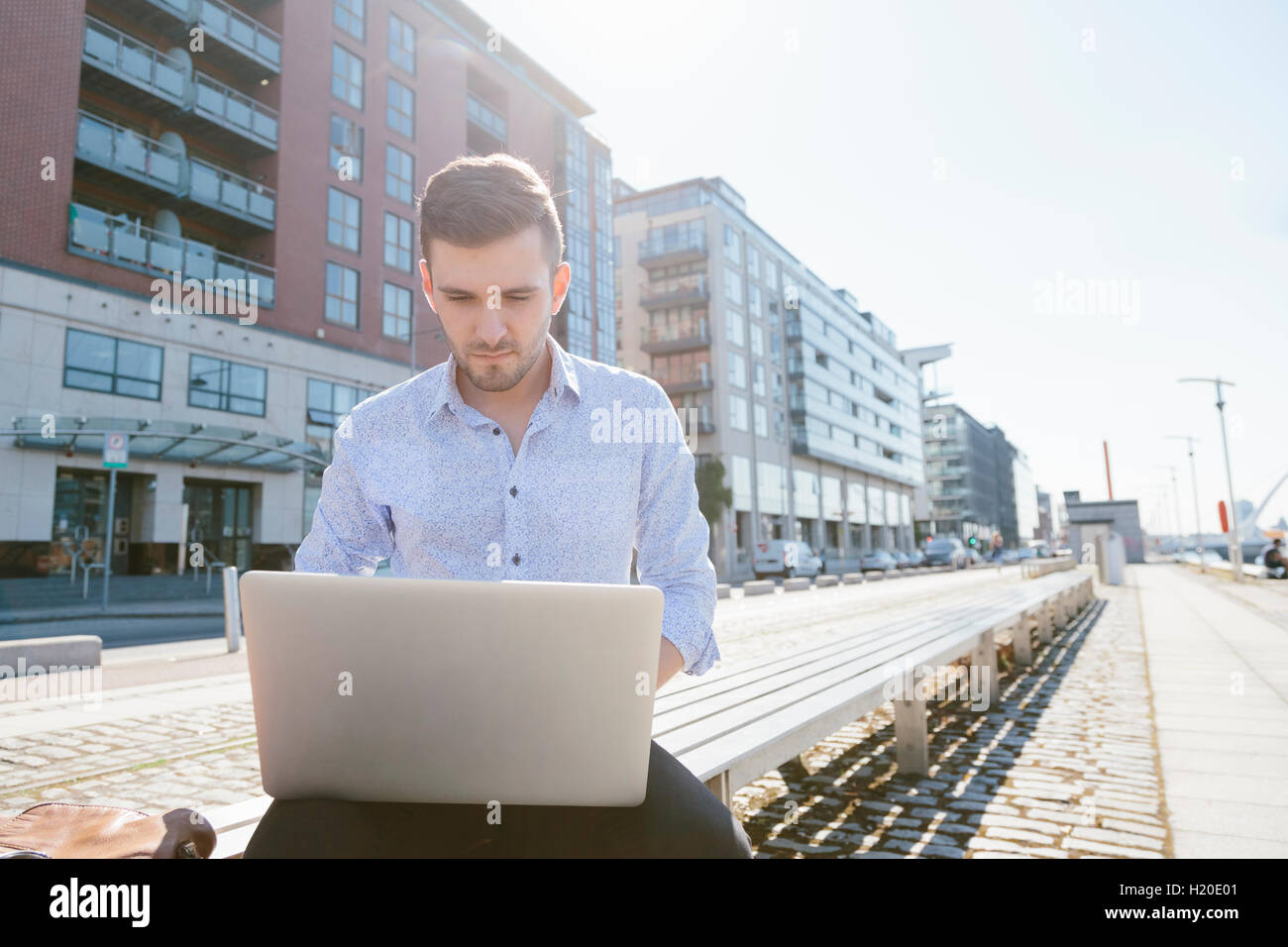Young businessman sitting on bench using laptop Stock Photo - Alamy