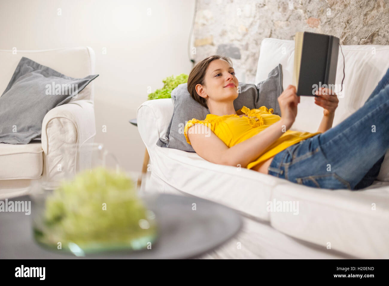 Woman lying on couch, reading a book Stock Photo