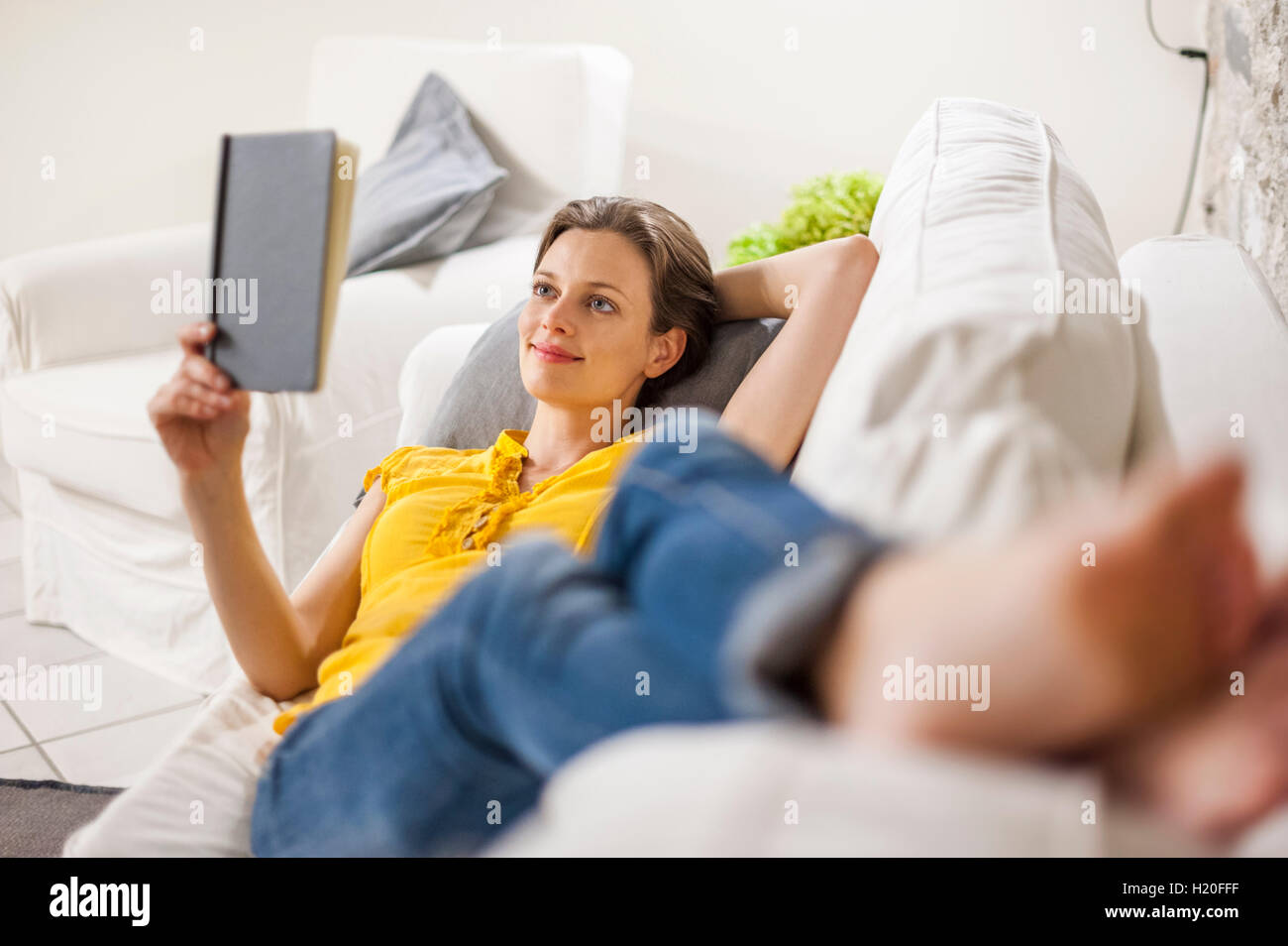 Woman lying on couch, reading a book Stock Photo