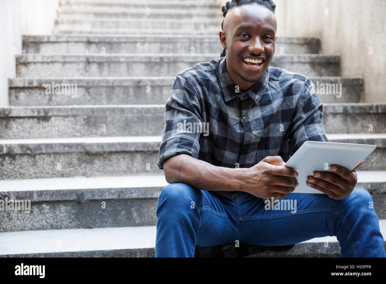 Young man sitting on stairs, using digital tablet Stock Photo - Alamy