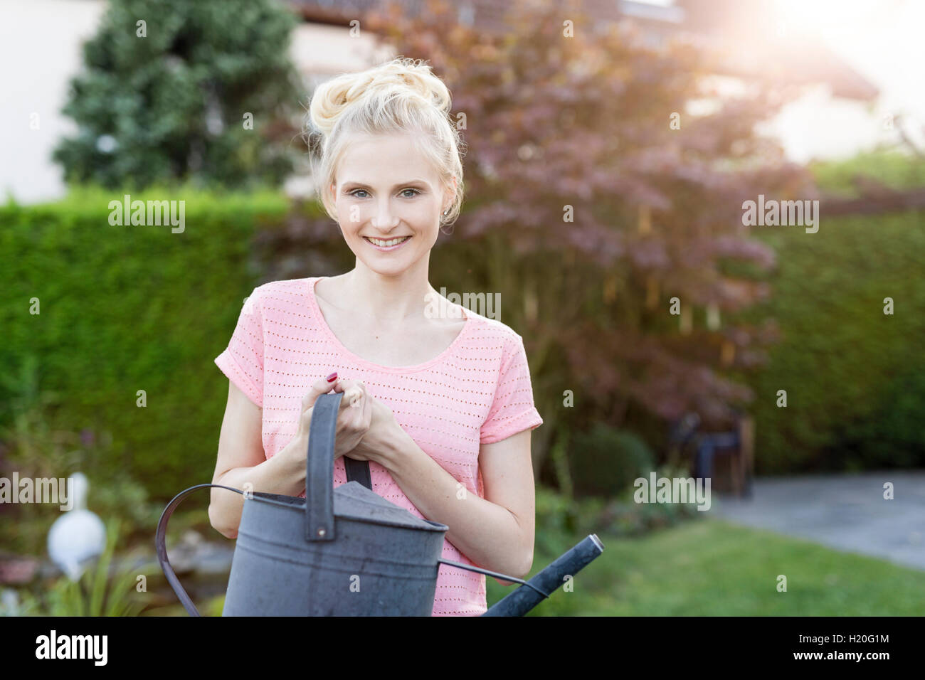 Portrait of blond woman holding watering can in garden Stock Photo - Alamy