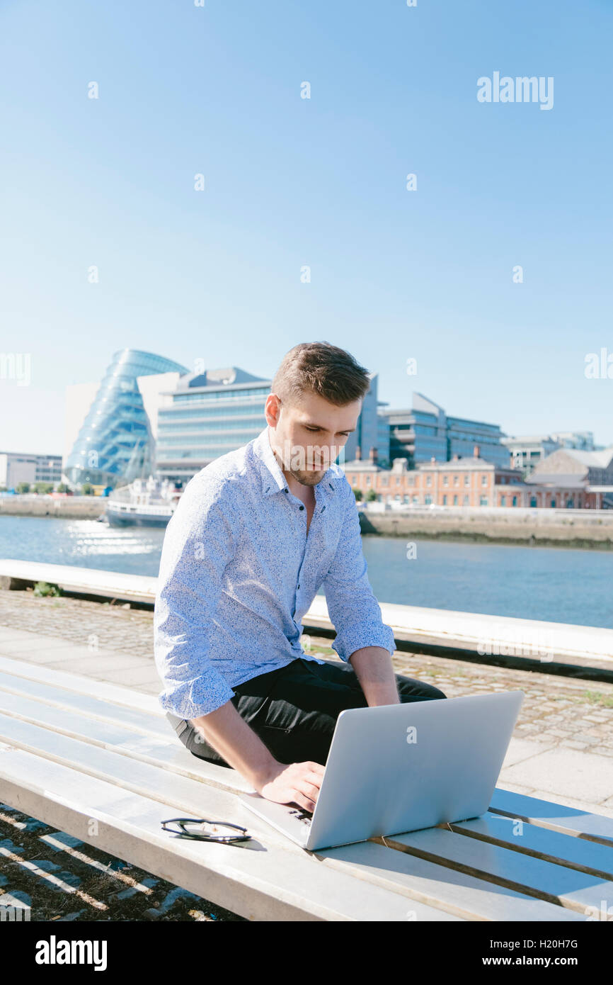 Ireland, Dublin, young businessman sitting on bench using laptop Stock ...