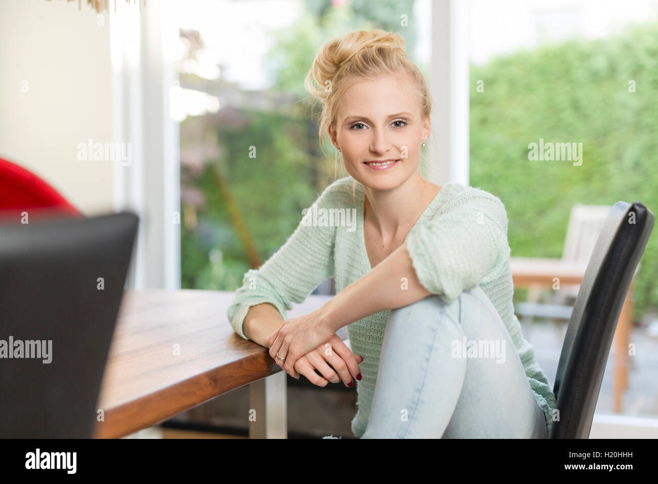 Portrait of smiling blond woman sitting at dining table Stock Photo - Alamy