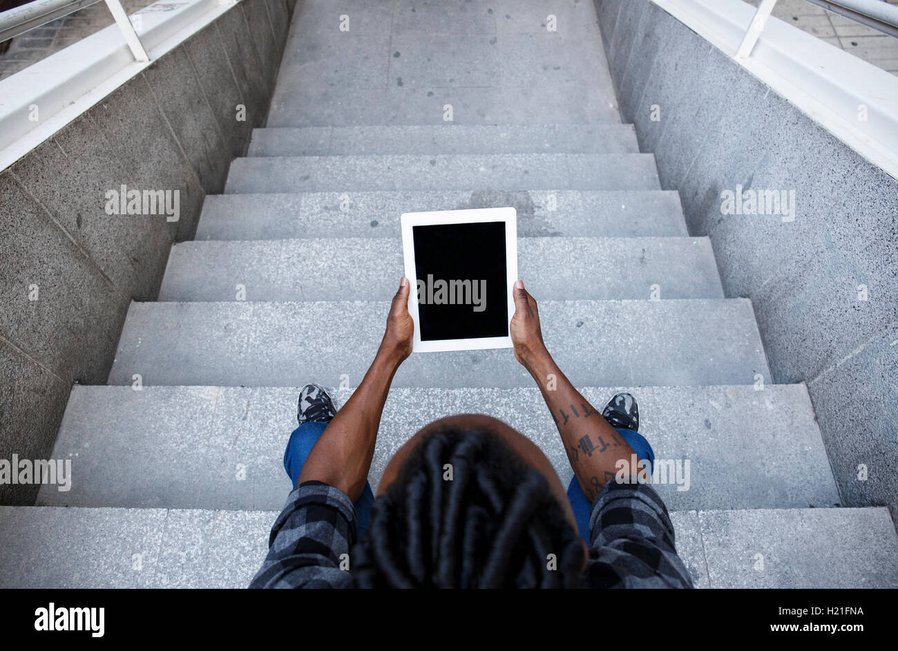 Young man sitting on stairs, using digital tablet Stock Photo - Alamy