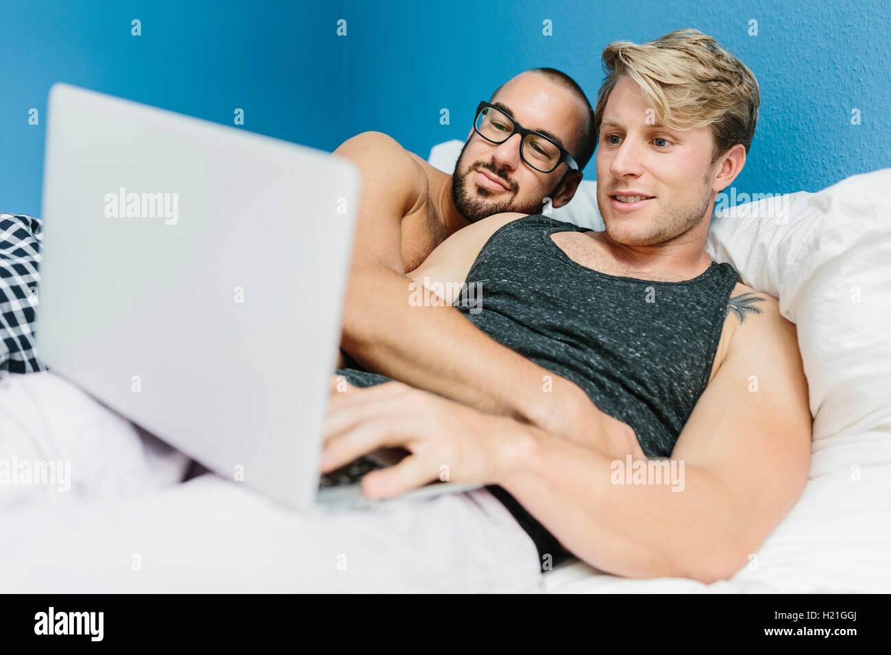 Gay couple lying in bed, using laptop Stock Photo