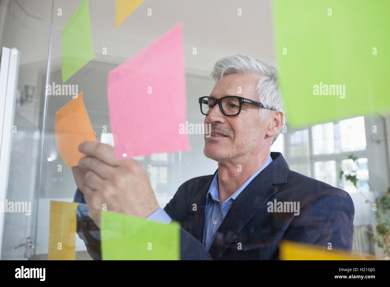 Businessman in office attaching adhesive notes at glass pane Stock Photo