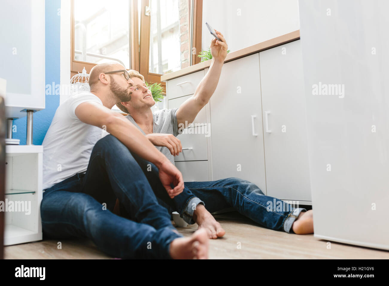 Gay couple sitting on floor, taking selfie Stock Photo