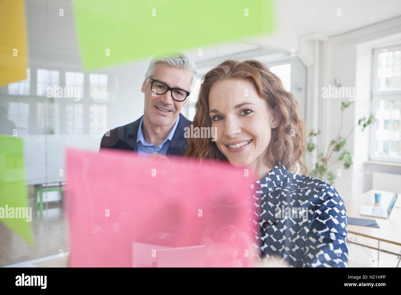 Businessman and woman looking at adhesive notes at glass pane Stock Photo