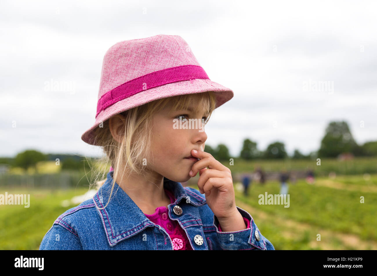 Portrait of pensive little girl wearing pink hat on a strawberry field