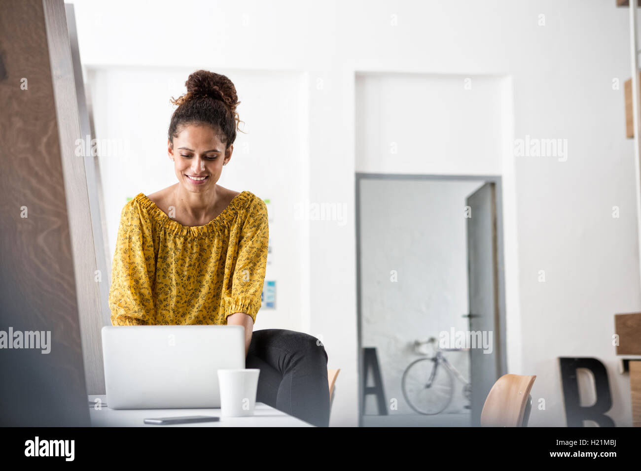 Smiling woman sitting on office desk using laptop Stock Photo