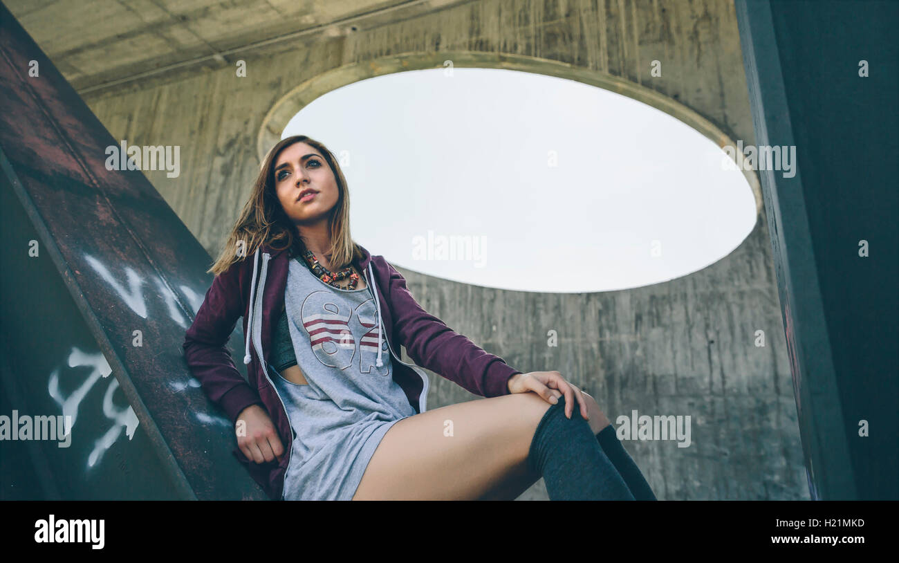 Young woman wearing hooded jacket and stockings sitting on pillar Stock Photo Alamy