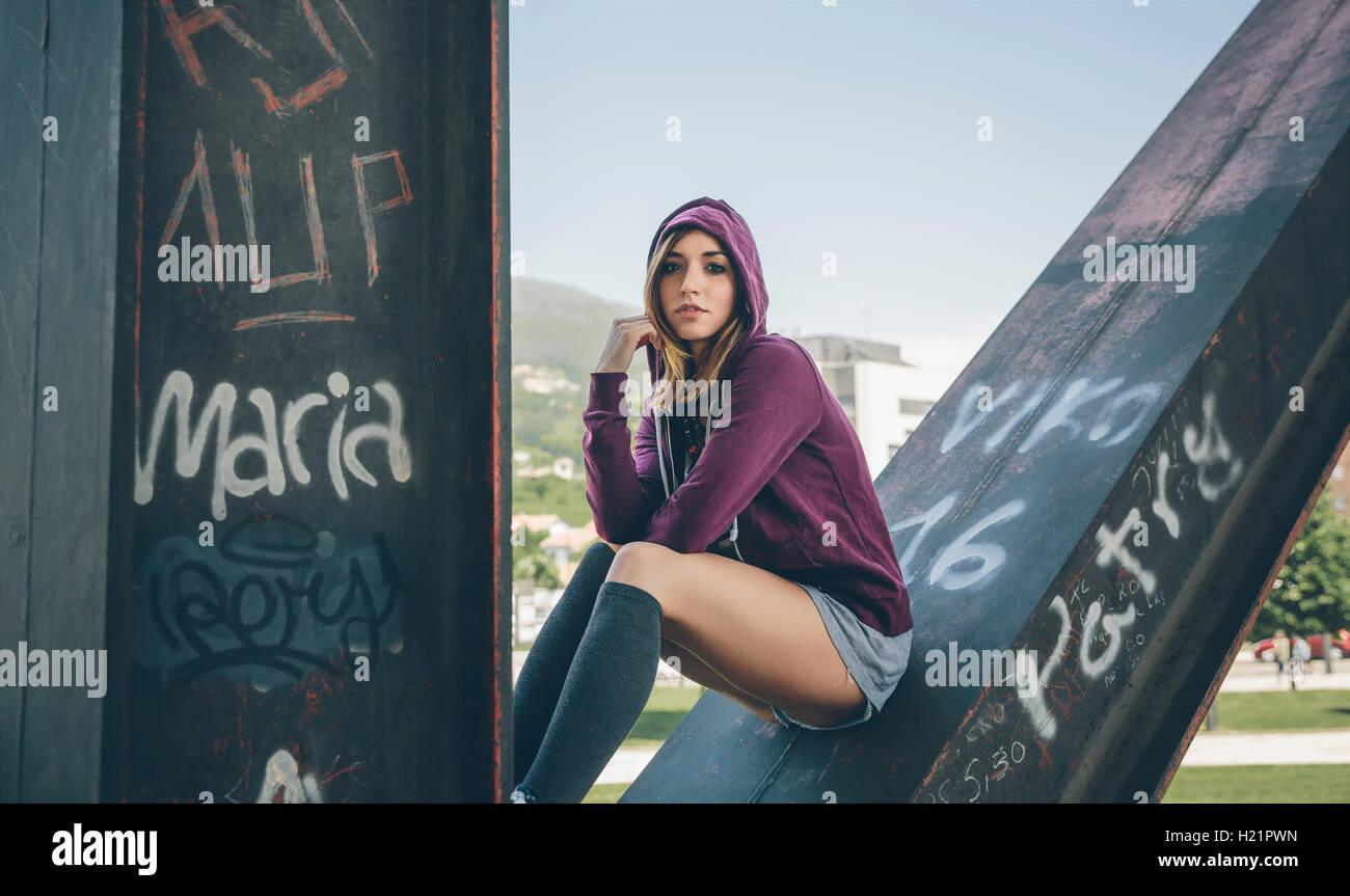 Young woman wearing hooded jacket and stockings sitting on pillar Stock Photo Alamy